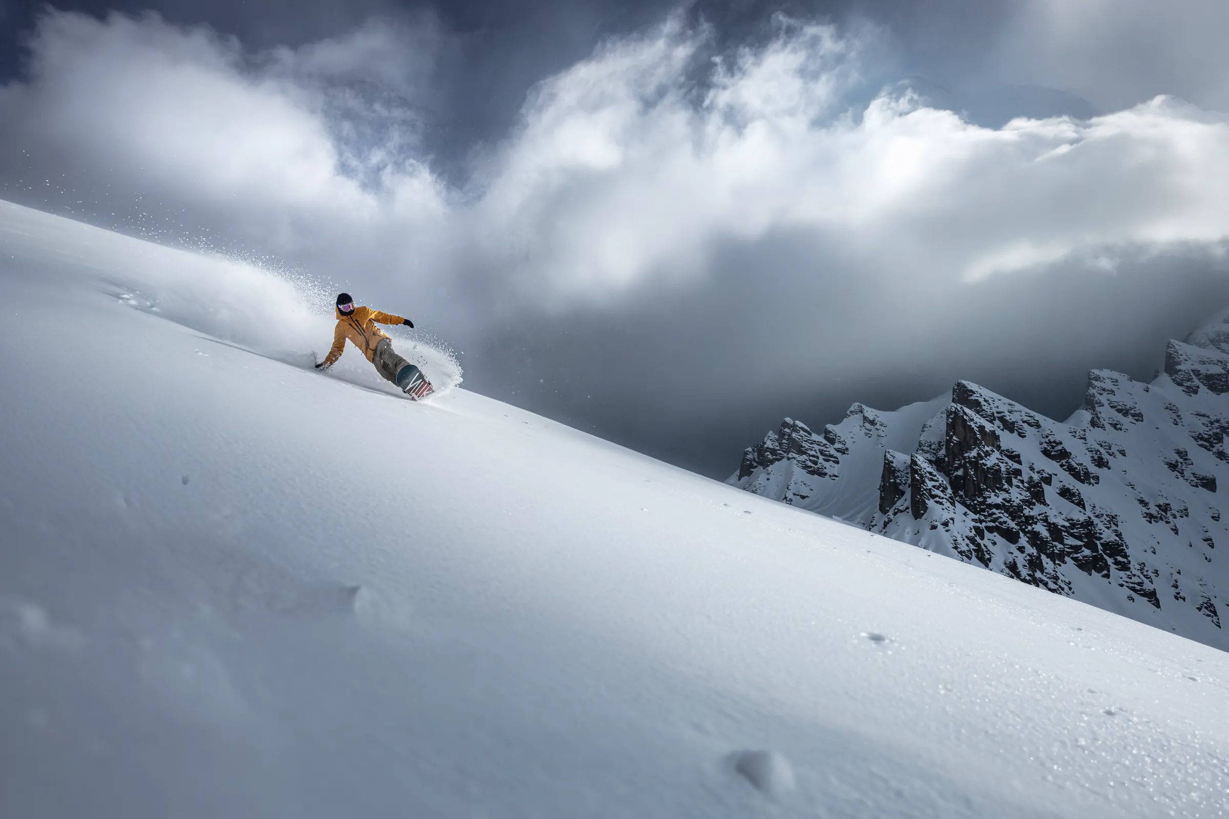 Un snowboarder trazando una curva en nieve polvo bajo una cresta rocosa